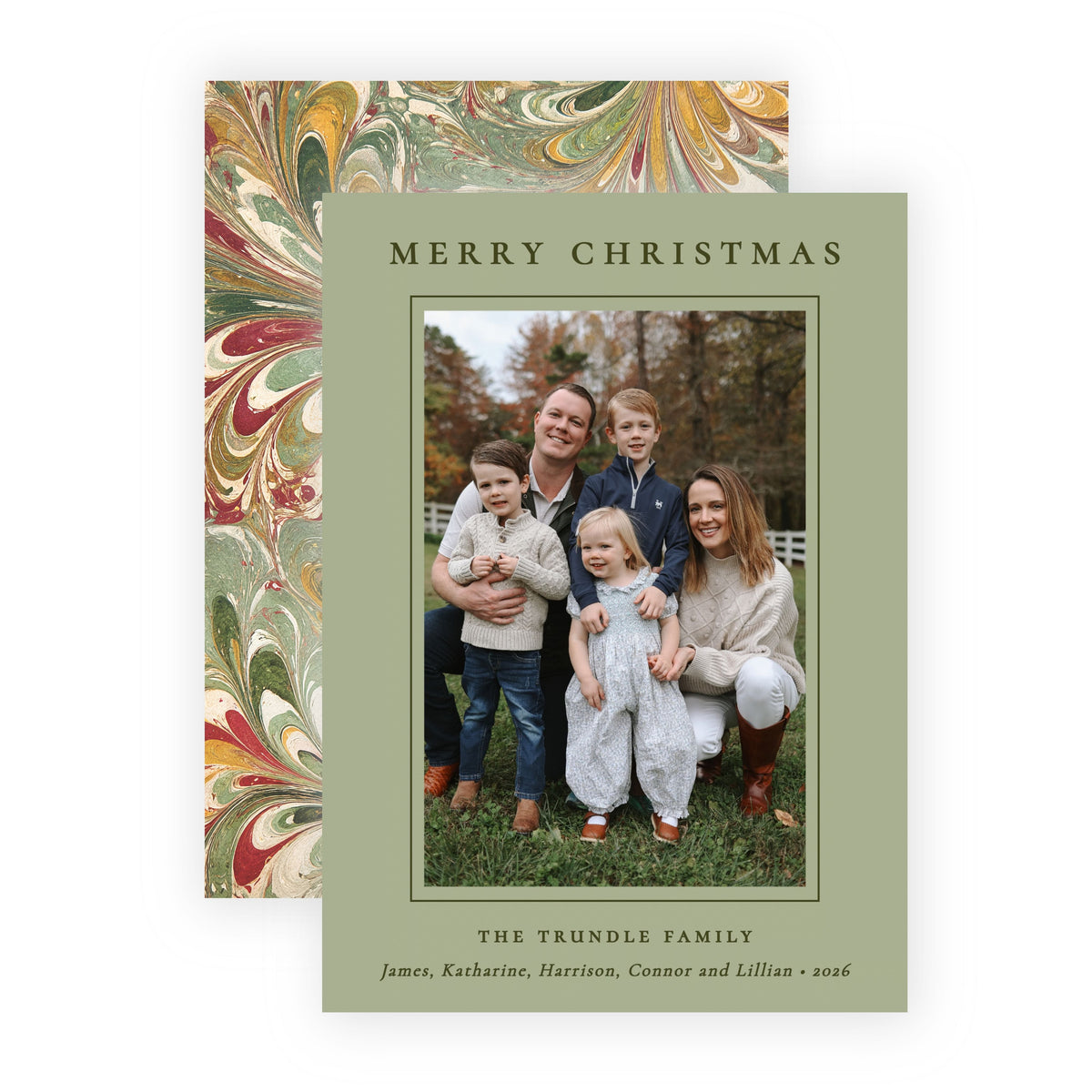 A personalized Christmas family photo card with a sage green border and a central family portrait, shown in front of a matching patterned envelope with red, gold, and green marbled design on a white background.
