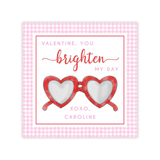 The image is a Valentine's Day card with a pink and white checkered border. The card features a pair of red heart-shaped sunglasses and a message that reads "Valentine, you brighten my day" in a cursive font.