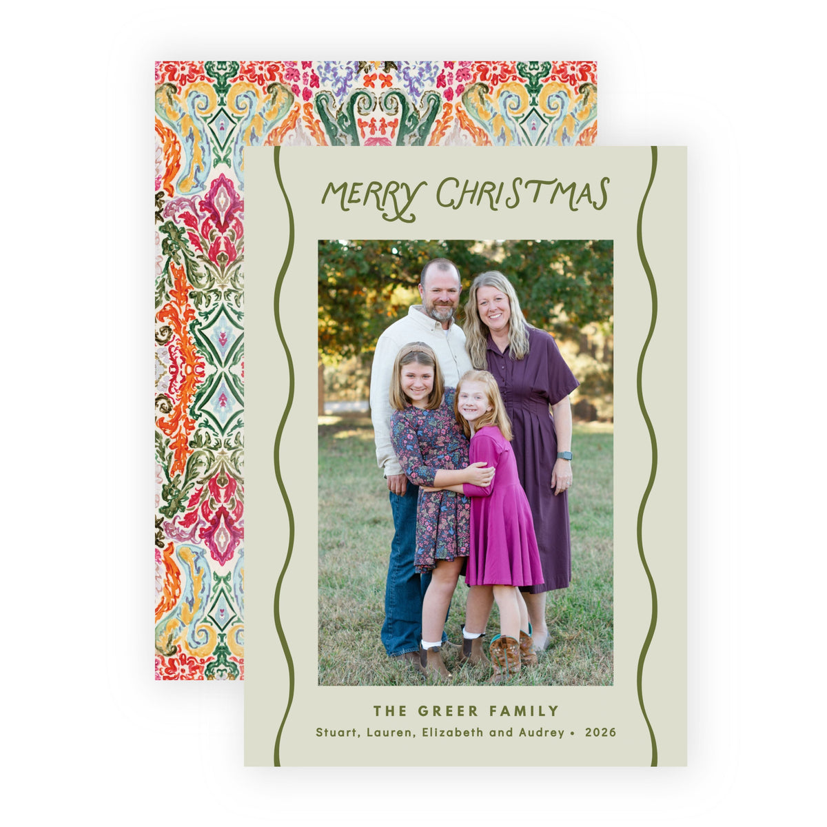 A personalized Christmas family card with a cream background, green wavy border lines, and the text 'Merry Christmas' and 'The Greer Family' printed on it. The card is shown in front of a matching patterned envelope with a multicolor geometric design.