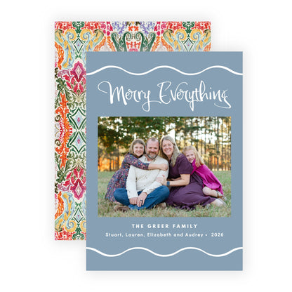 A personalized holiday greeting card with a slate blue front and a colorful patterned back, shown on a clean white background. The front features a photo of a family and the text 'Merry Everything' and 'The Green Family'.