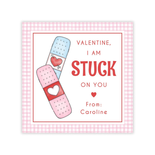 The image is a Valentine's Day card with a pink and white checkered border. The card features a pair of bandages with a heart symbol on them, and a message that reads "Valentine, I am STUCK on you From: Caroline".