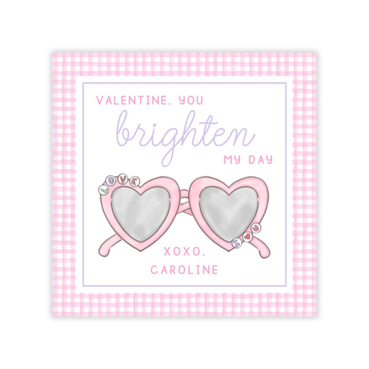 The image is a Valentine's Day card with a pink and white checkered border. The card features a pair of heart-shaped sunglasses with a message that reads "Valentine, you brighten my day" and "XOXO, CAROLINE".